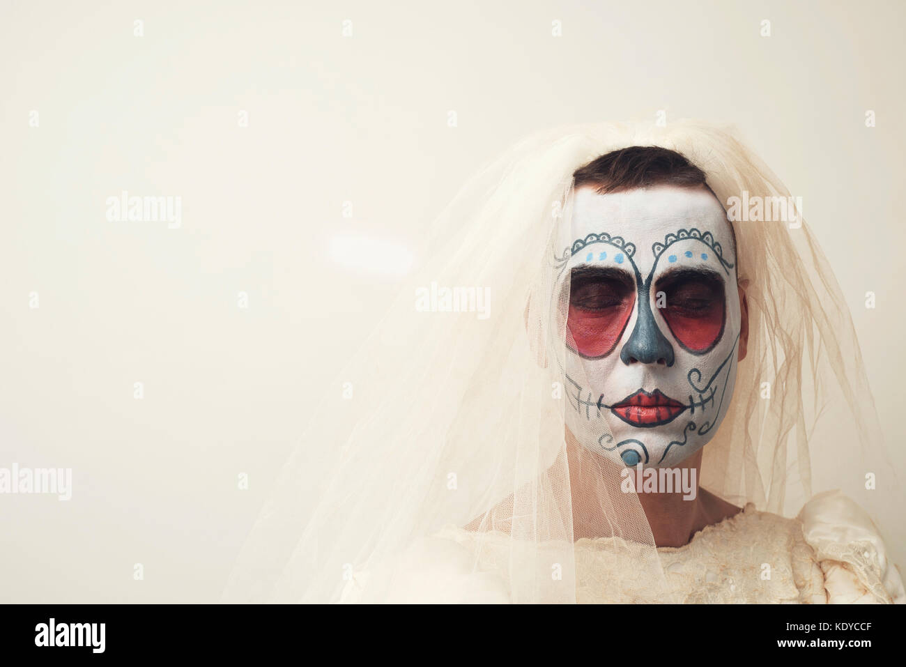 Primo piano di una persona con capelli corti in un abito da sposa con un messicano calaveras trucco, indossando il velo contro un fondo bianco con uno spazio vuoto Foto Stock