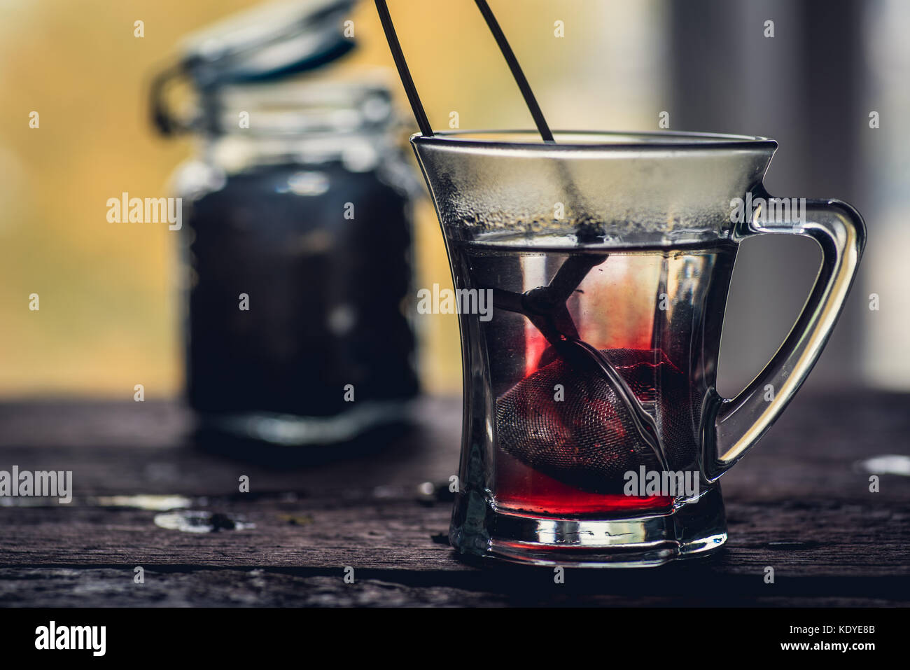 Bicchiere di rosso o di nero di tè o di erbe in stainer tè sul tavolo di legno Foto Stock