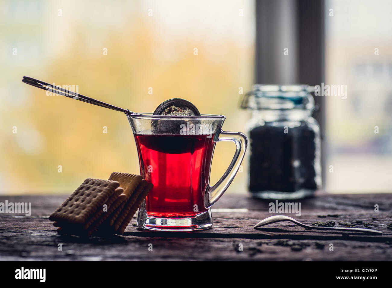 Bicchiere di rosso o di nero di tè o di erbe in stainer tè sul tavolo di legno Foto Stock
