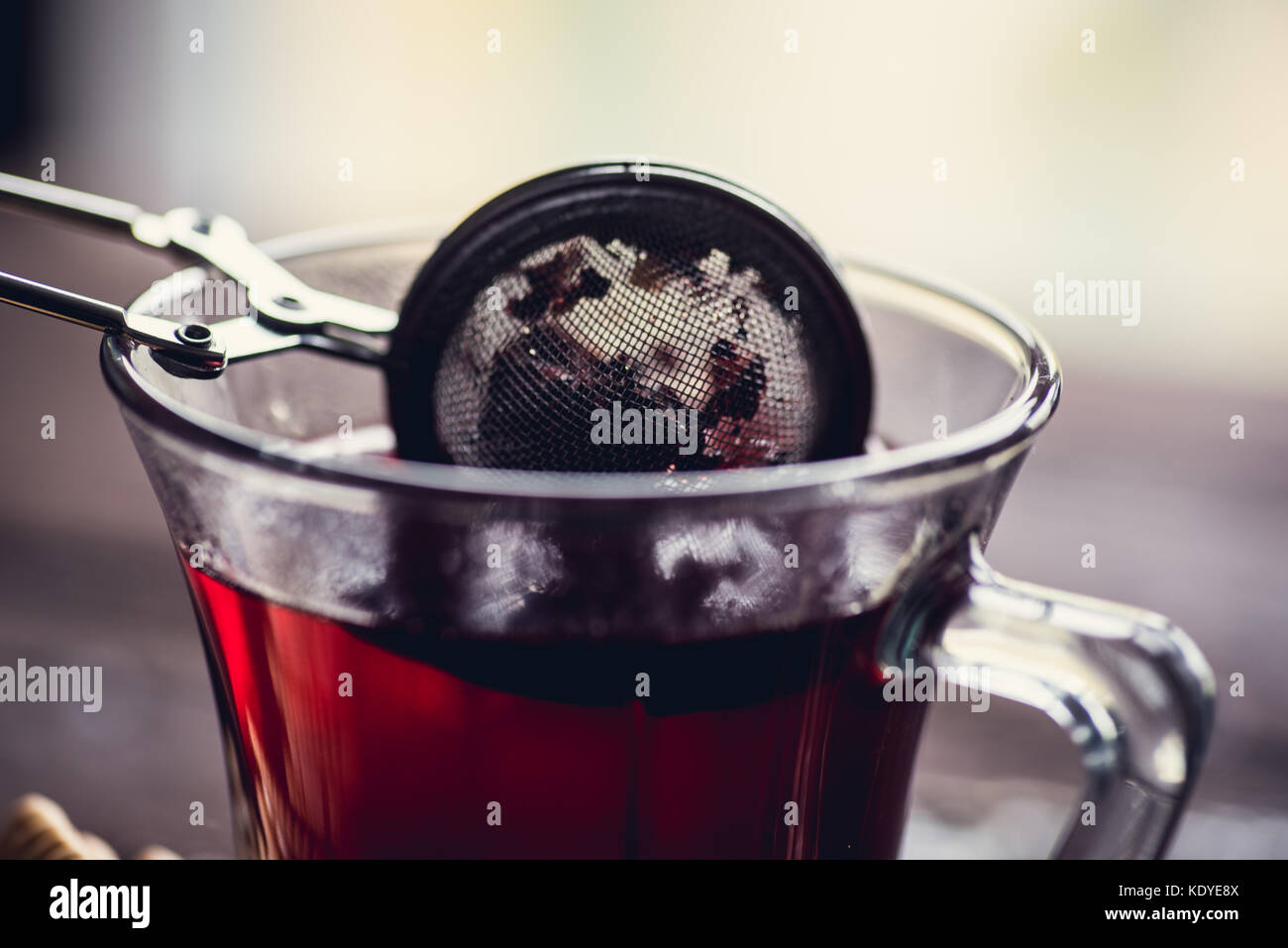 Bicchiere di rosso o di nero di tè o di erbe in stainer tè sul tavolo di legno Foto Stock