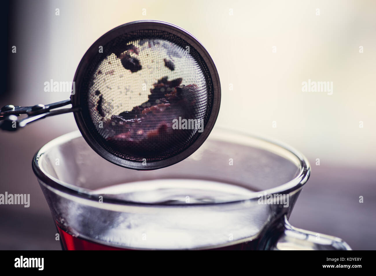 Bicchiere di rosso o di nero di tè o di erbe in stainer tè sul tavolo di legno Foto Stock