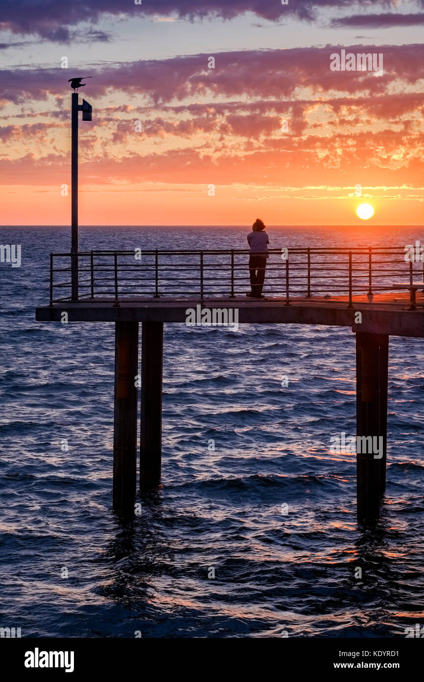 Un lone persona gode di un magnifico tramonto al mare di Adelaide del molo di Brighton su una mite serata d'estate. Foto Stock