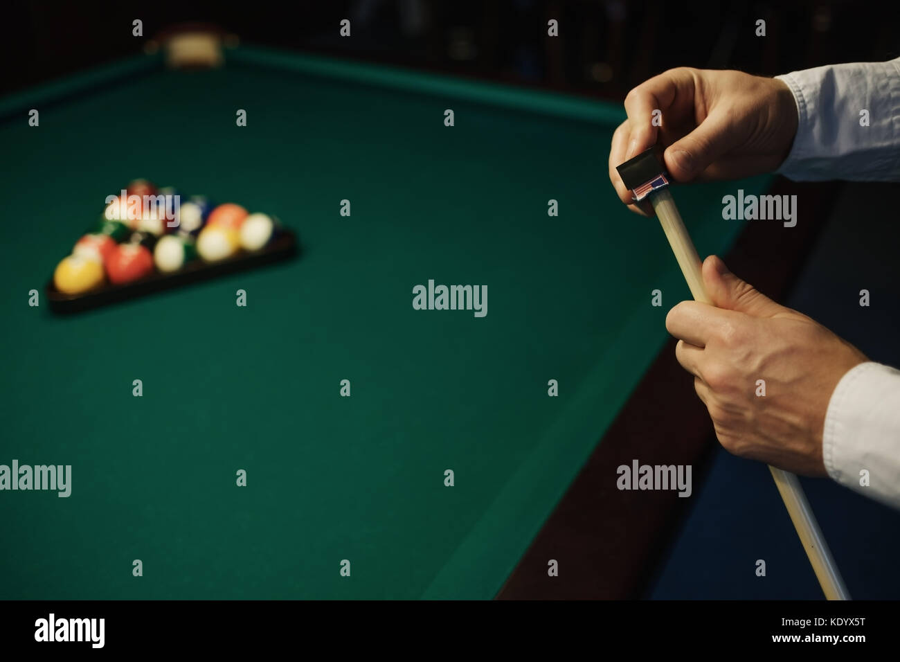Uomo caucasico wipes una stecca con chalk pronto per iniziare il gioco. Foto Stock