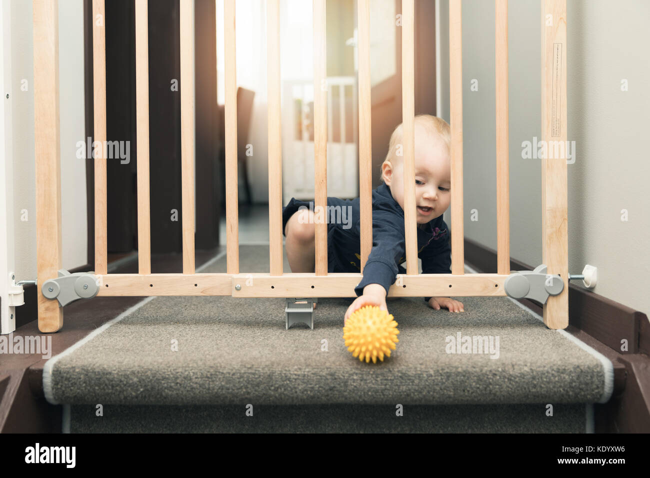 Bambino che gioca dietro i cancelli di sicurezza anteriore di scale a casa Foto Stock