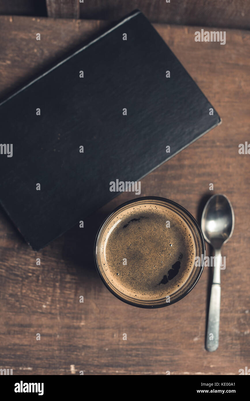 Bicchiere di bevanda caffè, vecchio libro e cucchiaio su tavola in legno rustico Foto Stock