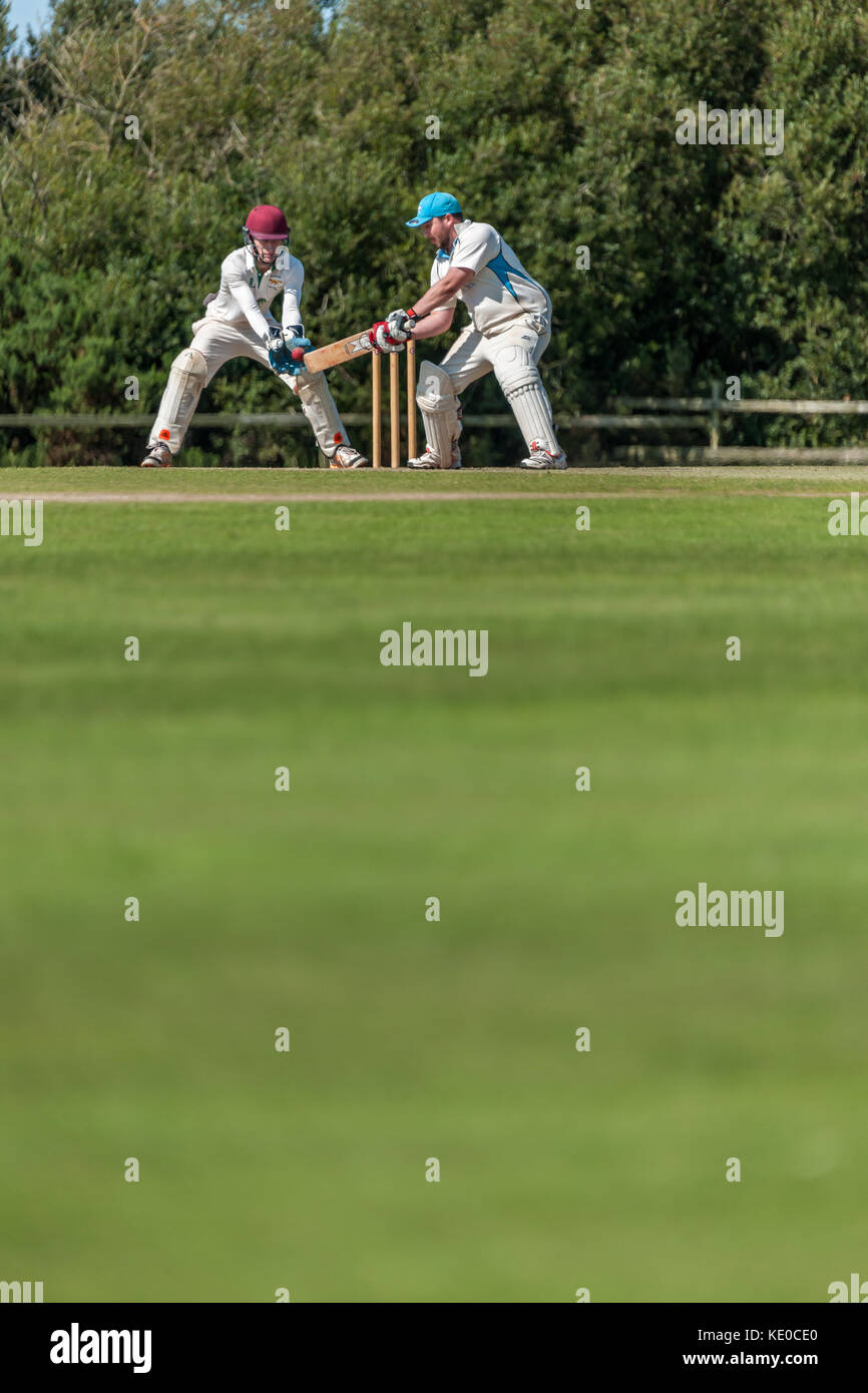 Un battitore gioca un colpo durante una domenica League match tra due locali squadre di cricket. Foto Stock