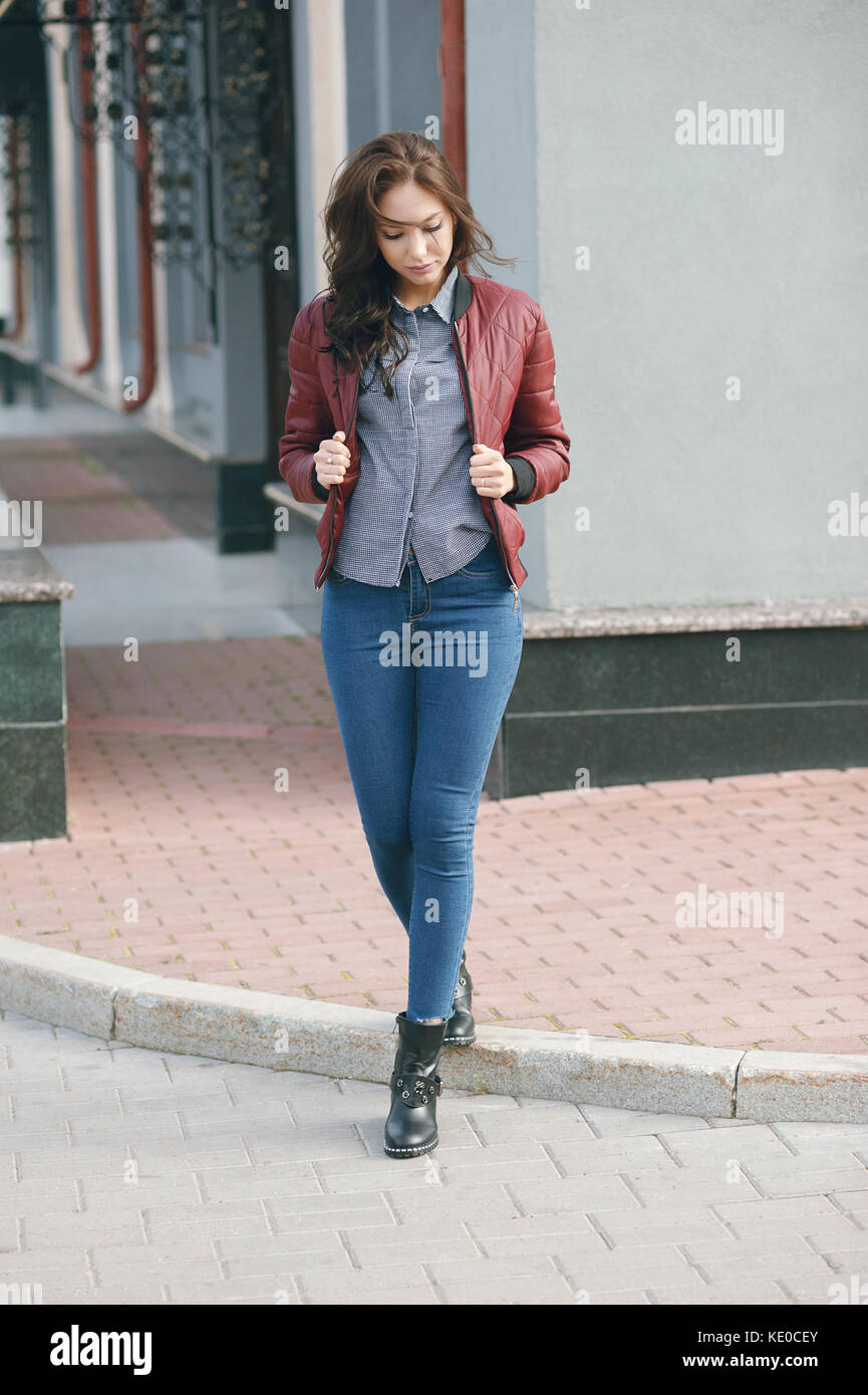 Giovane bella donna elegante in un pilota di borgogna giacca e jeans blu street style Primavera e autunno trend guardare capelli al vento Foto stock Alamy