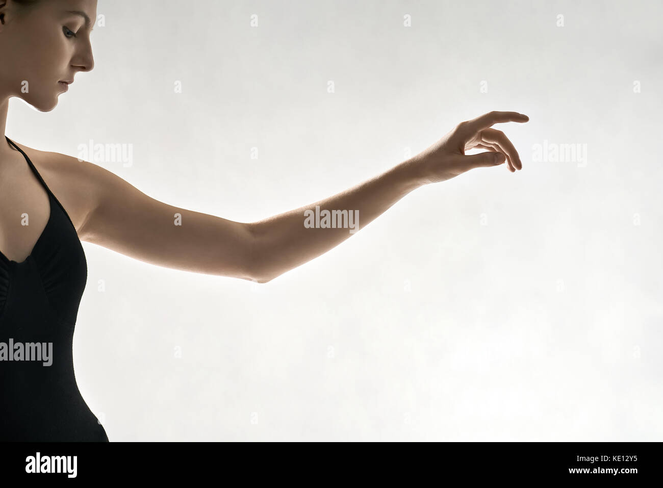 Deliziosa ballerina è in posa in studio sullo sfondo luminoso. Ha conseguito il suo braccio sinistro in aria e guarda verso il basso. bambina indossa un nero leotard Foto Stock