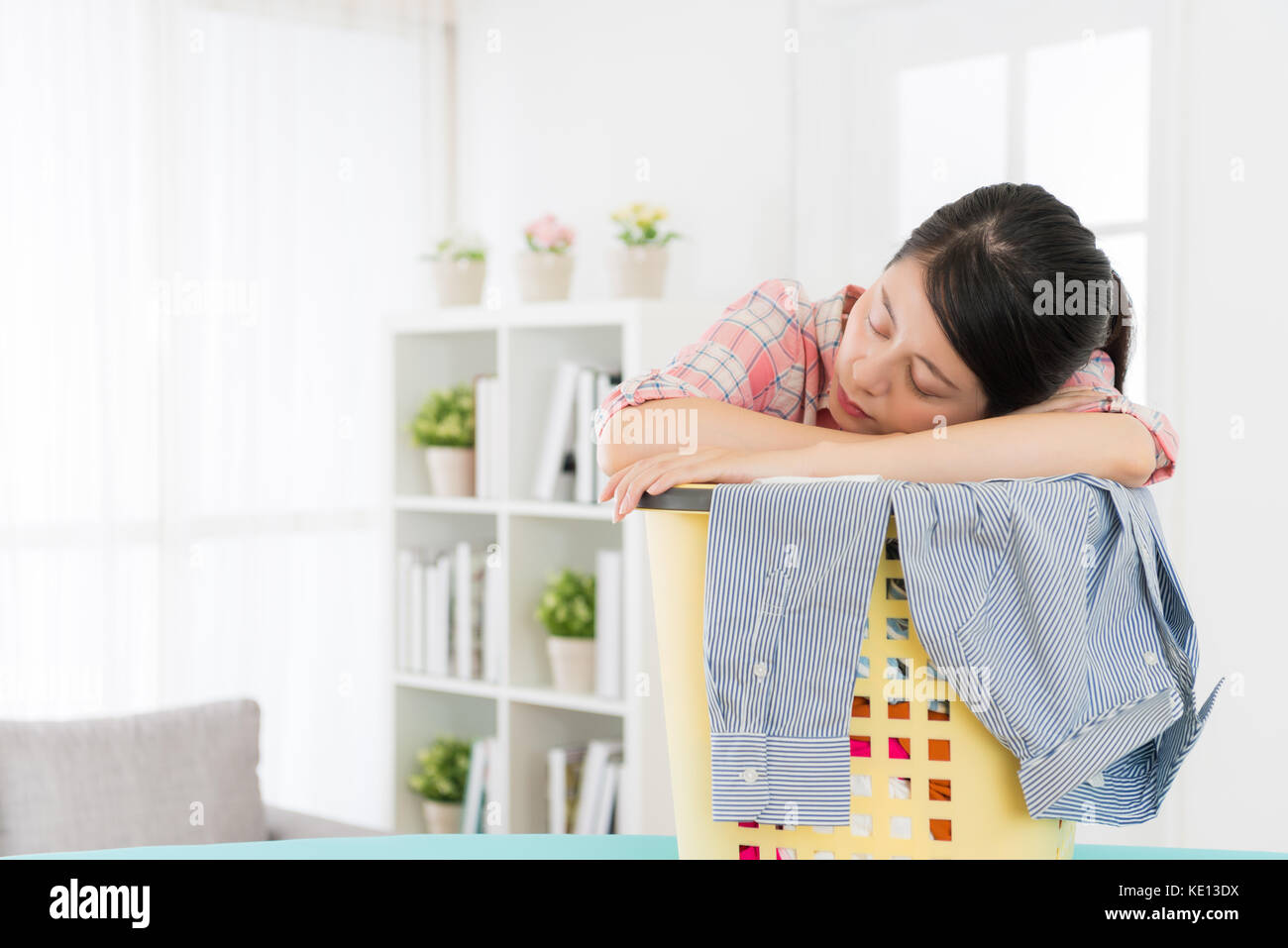 Giovane bella donna che dorme sul cesto per la biancheria quando lei a fare  le pulizie e azienda di abbigliamento disordinati in salotto pronto per  ordinare i miei vestiti Foto stock -