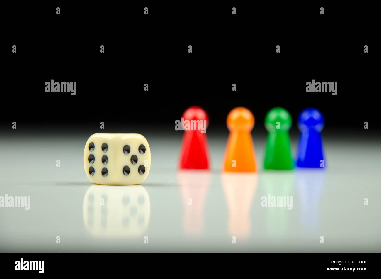 Vista ravvicinata di una fila di figure colorate sul retro con una riproduzione di cubo su una sfocata a bianco su sfondo nero con la riflessione Foto Stock