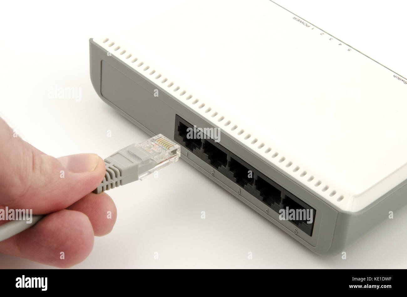 Una vista ravvicinata di un dito della mano di un collegamento grigio cavo lan al router su sfondo bianco Foto Stock