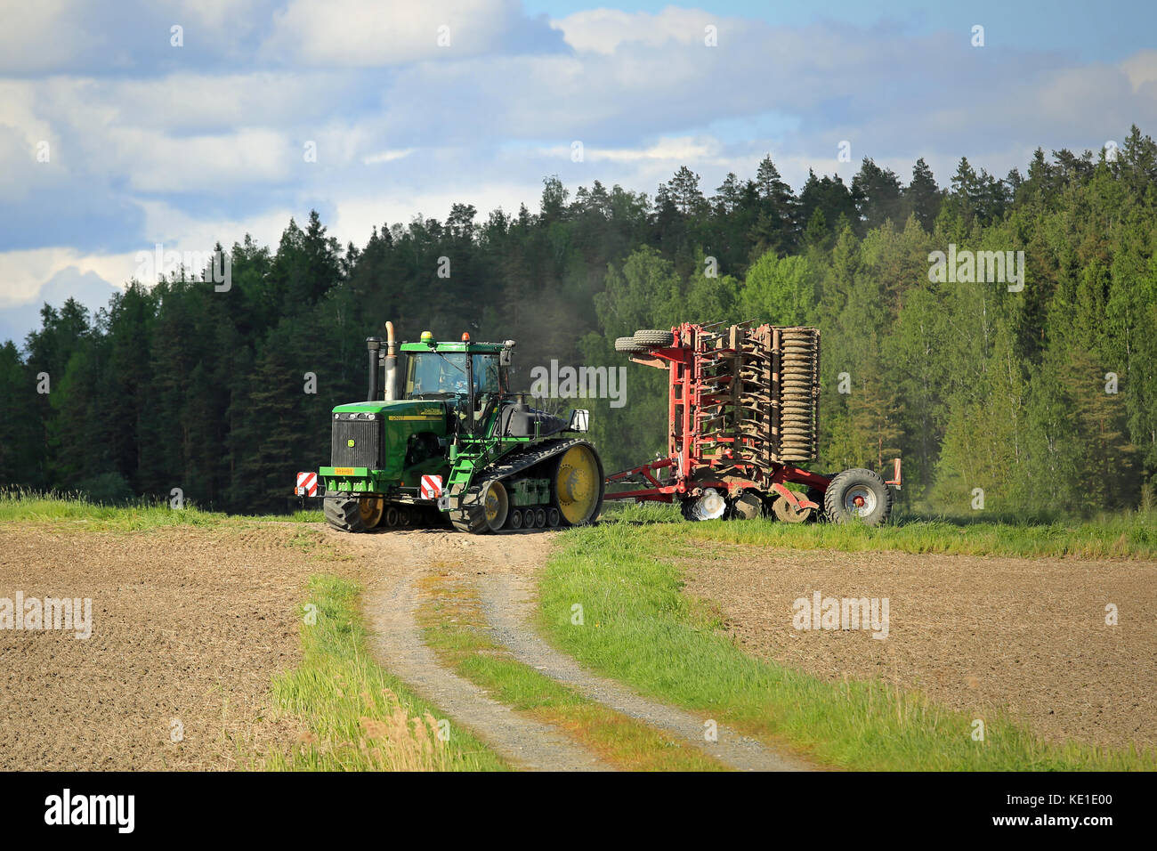 SALO, FINLANDIA - 27 MAGGIO 2016: Trattore cingolato agricolo John Deere 9520T e coltivatore che si muove lungo la strada sterrata nel paesaggio rurale primaverile Foto Stock