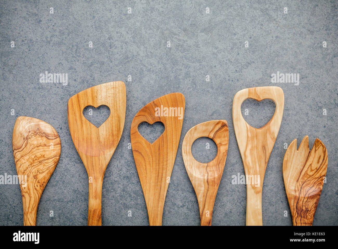 Legno di vari utensili da cucina confine. cucchiai di legno e la spatola di legno scuro su sfondo di pietra con piatto di laici e di spazio copia. Foto Stock