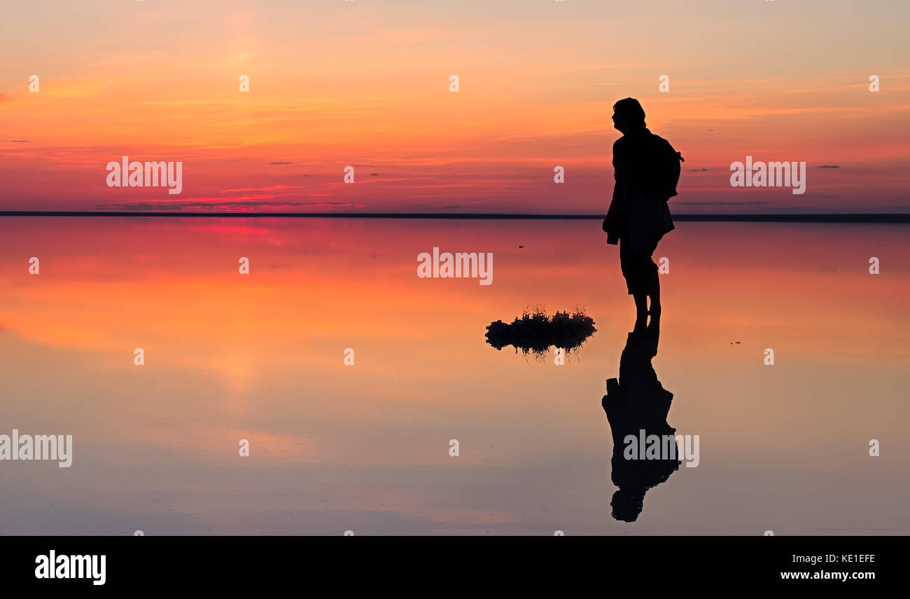 Silhouette di un solo uomo che guarda verso la vibrante tramonto riflesso in acque poco profonde di solt lago Foto Stock