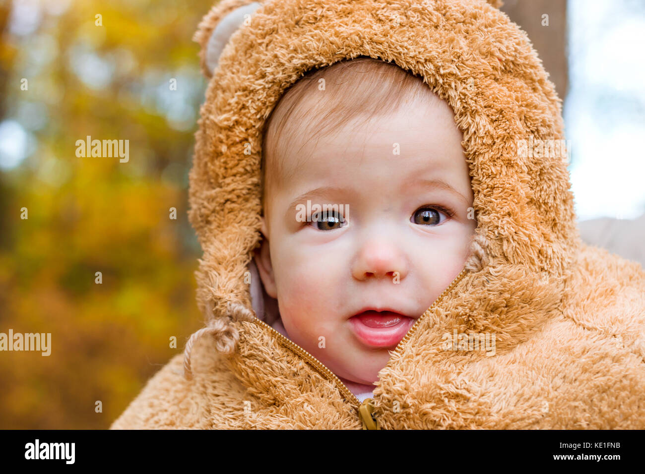 Baby in posa sullo sfondo del parco d'autunno. bambino vestito in caldi stilizzata di Teddy bear costume, divertirsi in giardino luminoso inizio autunno. famiglia a piedi in Foto Stock
