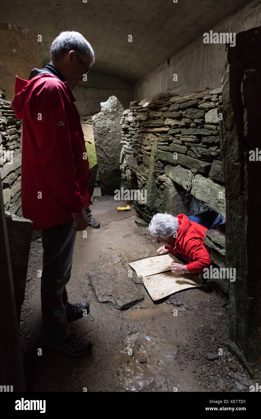 Tomba delle aquile, Ronaldsay meridionale, Isole Orcadi, Scozia, Regno Unito - un visitatore anziano entra gamely nella tomba utilizzando un sistema di trolley Foto Stock