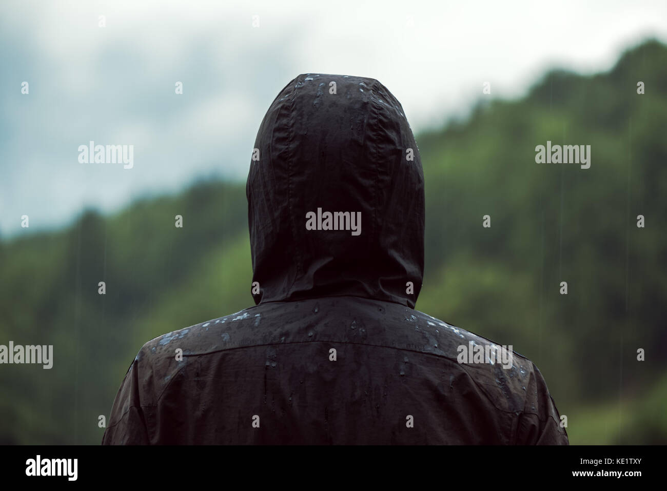 Vista posteriore del uomo incappucciato in piedi nella pioggia il freddo autunno nuvoloso giorno getting inzuppato Foto Stock