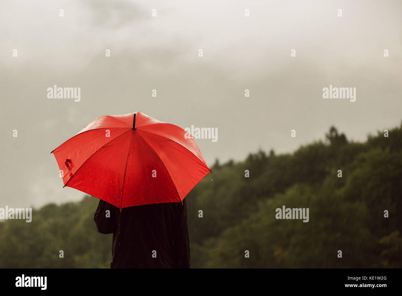 Uomo con ombrello rosso solitario in piedi sotto la pioggia e ottenere inzuppato Foto Stock