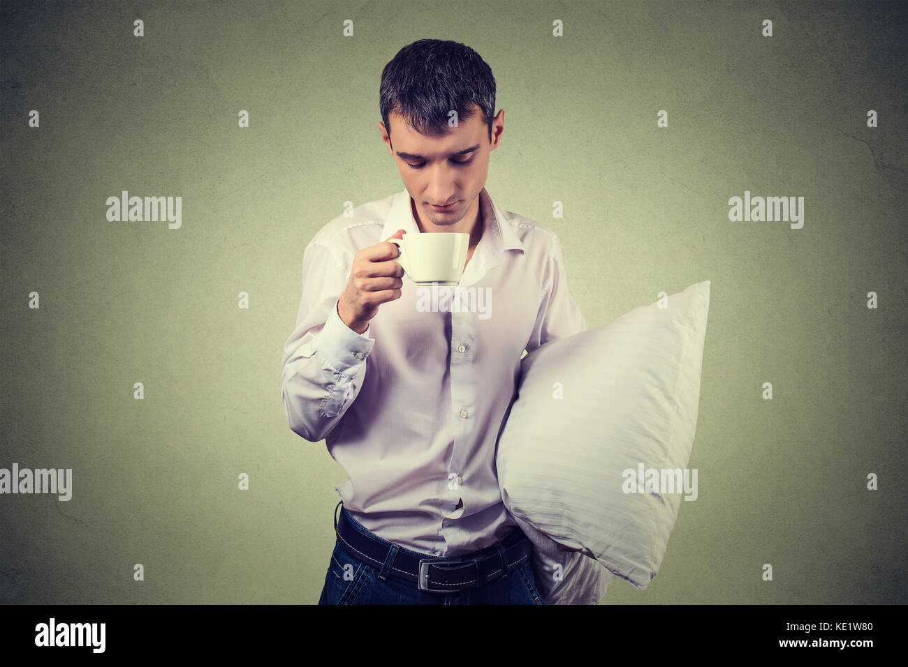 Molto stanco, quasi ad addormentarsi business man tenere una tazza di caffè e un cuscino lottando non crash e rimanere svegli, mantenendo i suoi occhi aperti, iso Foto Stock