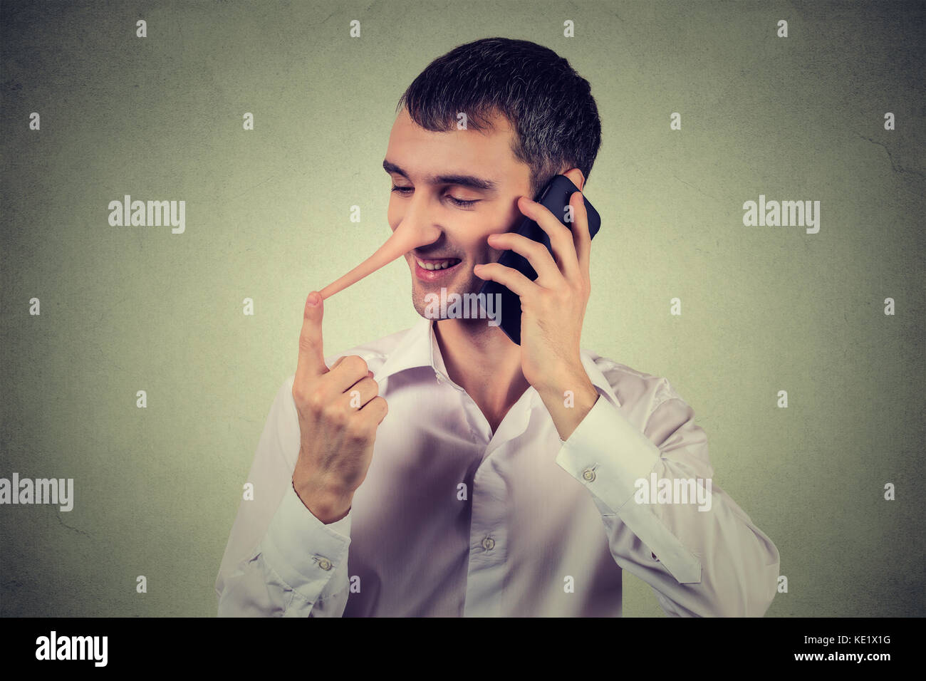 Bugiardo rappresentante del servizio clienti. Felice giovane con il naso lungo parlando al telefono cellulare isolata sul muro grigio Sfondo. bugiardo concetto umano. fac Foto Stock