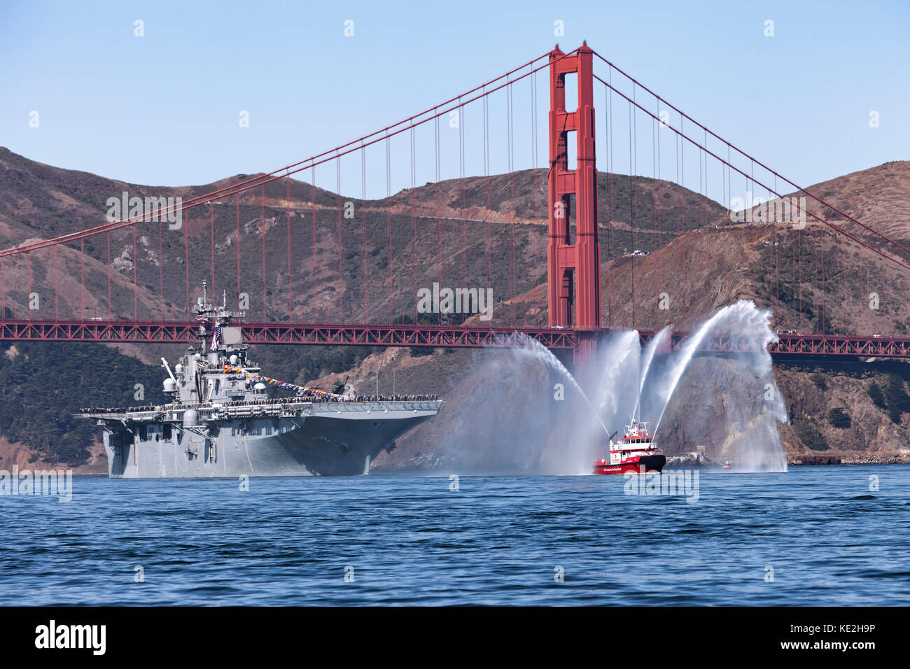 Marina degli Stati Uniti Wasp-classe assalto anfibio nave USS Essex (LHD-2) segue San Francisco Fireboat più recente attraverso il Golden Gate e su San F Foto Stock