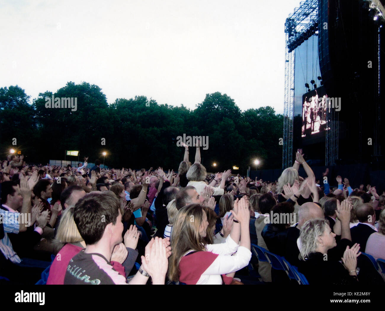 Udienza a Simon and Garfunkel concerto, "vecchi amici " tour, Hyde Park, Londra, 16 luglio 2004. American folk-rock duo formato 1964. Per la maggior parte persone di mezza età, grigio e bianco pelose fan in piedi, battendo le mani e agitando le mani. Foto Stock