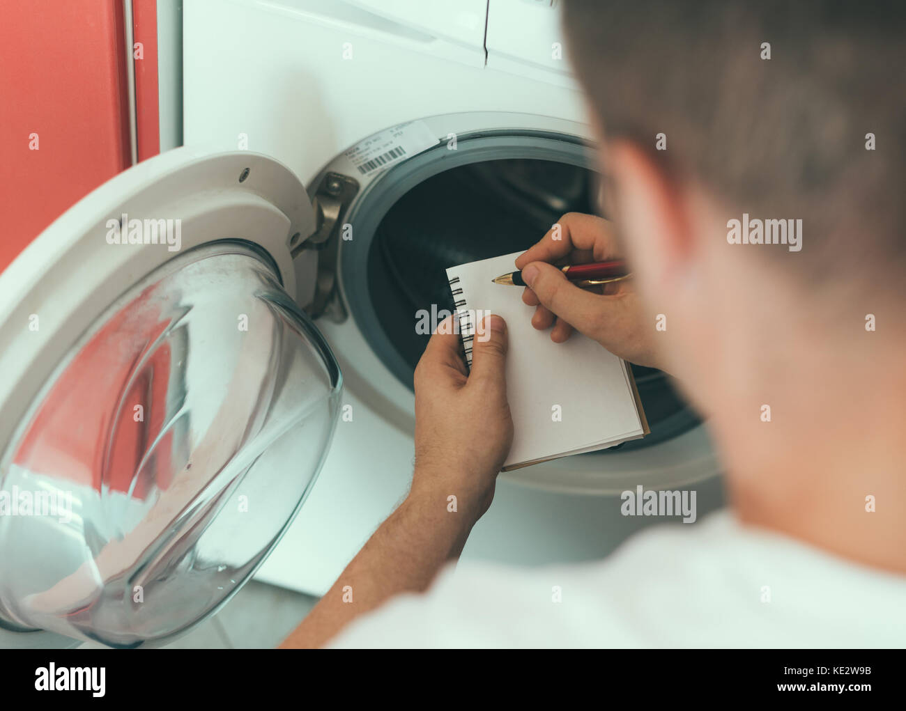 Tecnico maschile che ripara la lavatrice, scrivendo il codice del costruttore. Foto Stock