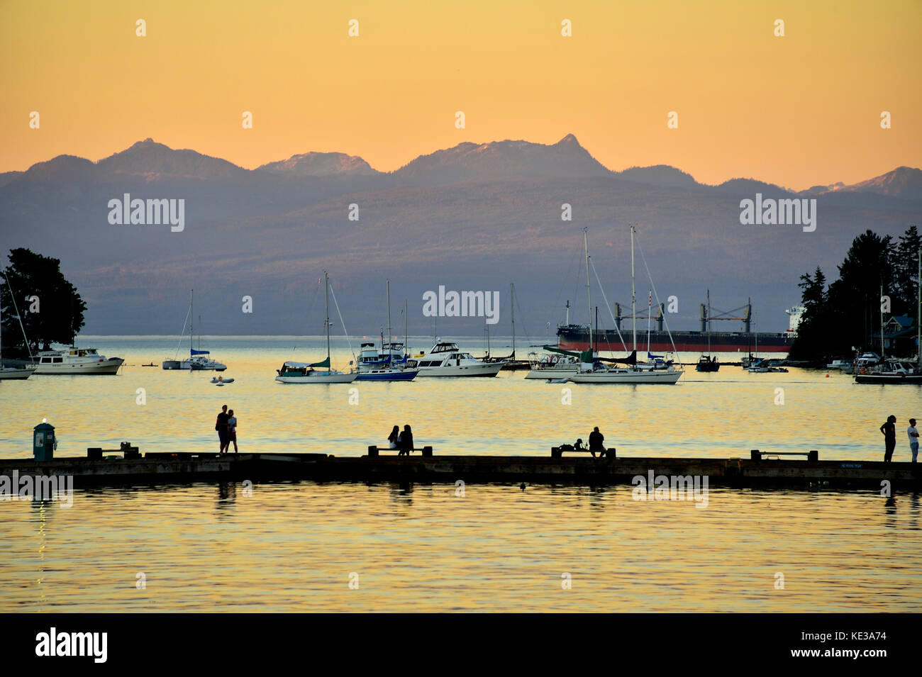 Porto di Nanaimo Vancouver Island ,b.c., con persone di pesca sul pontile di pesca e barche ormeggiate in acqua calma, contro uno sfondo di montagna Foto Stock