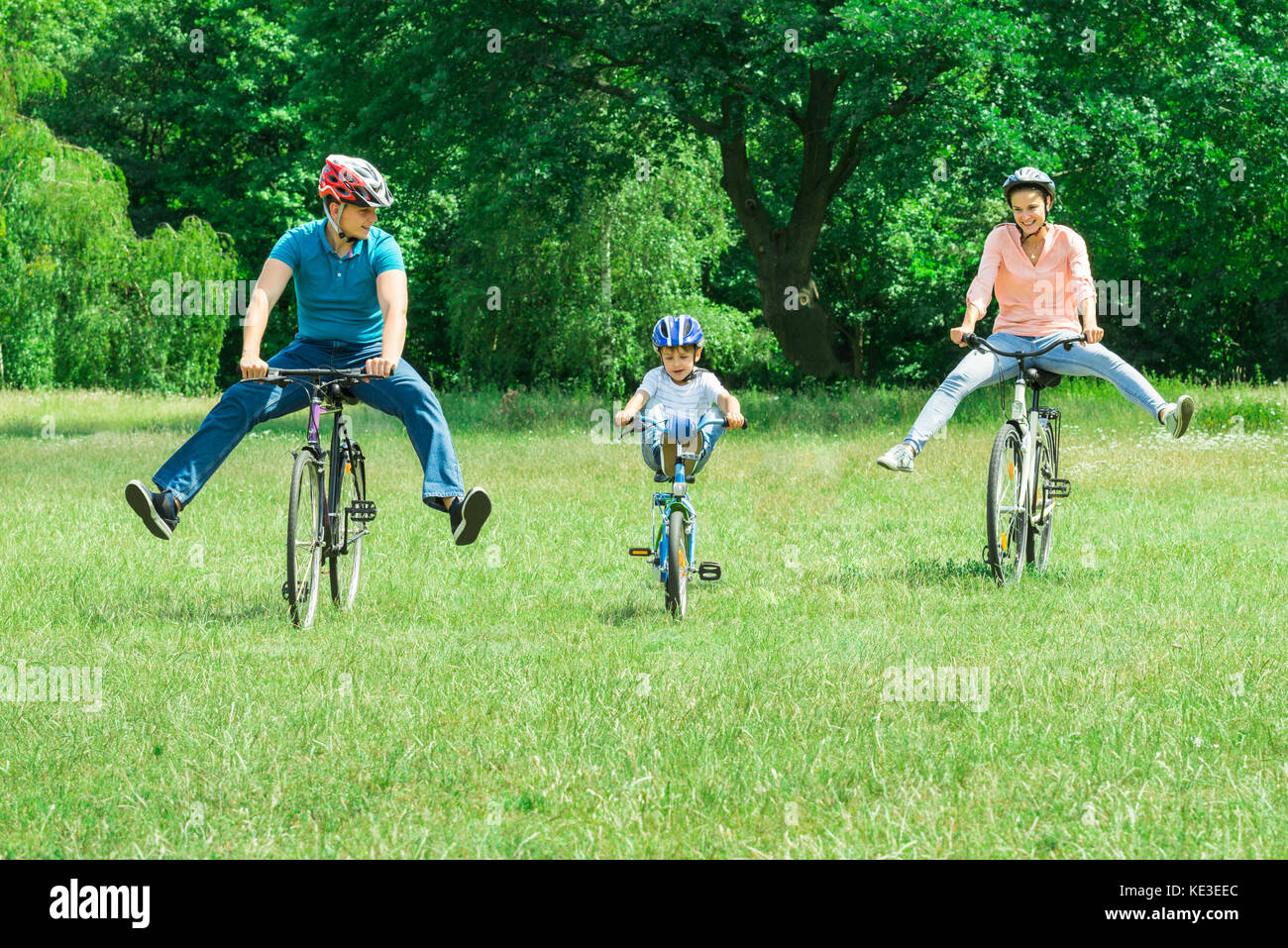 Felice ragazzo godendo di cavalcare in bicicletta nel parco con i suoi genitori Foto Stock