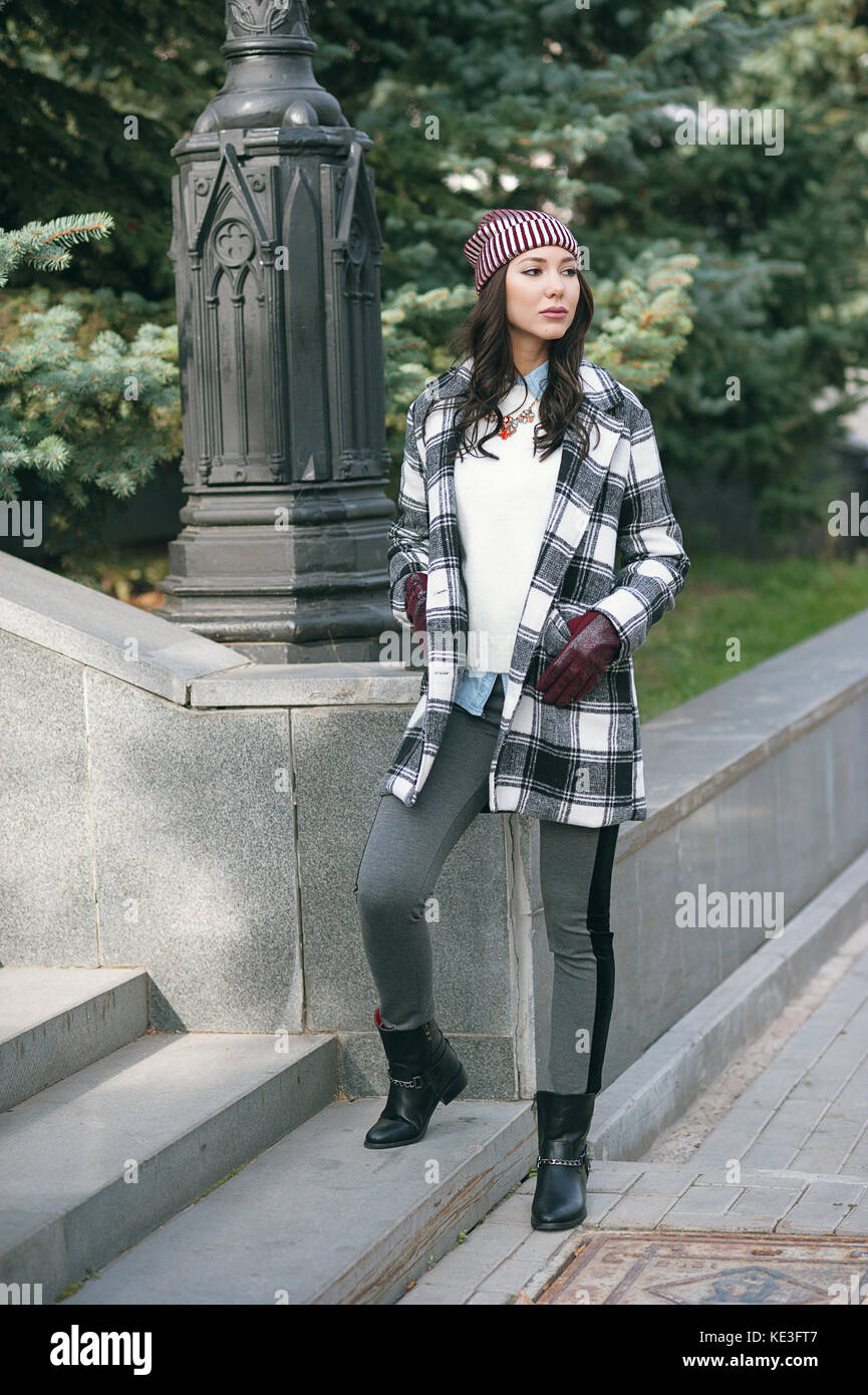 Giovane bella donna elegante, indossando un cappotto in un bianco e nero  gabbia, giacca bianco, grigio pantaloni, stivali neri. street style,  Primavera e autunno tendenza, un aspetto flirty Foto stock - Alamy