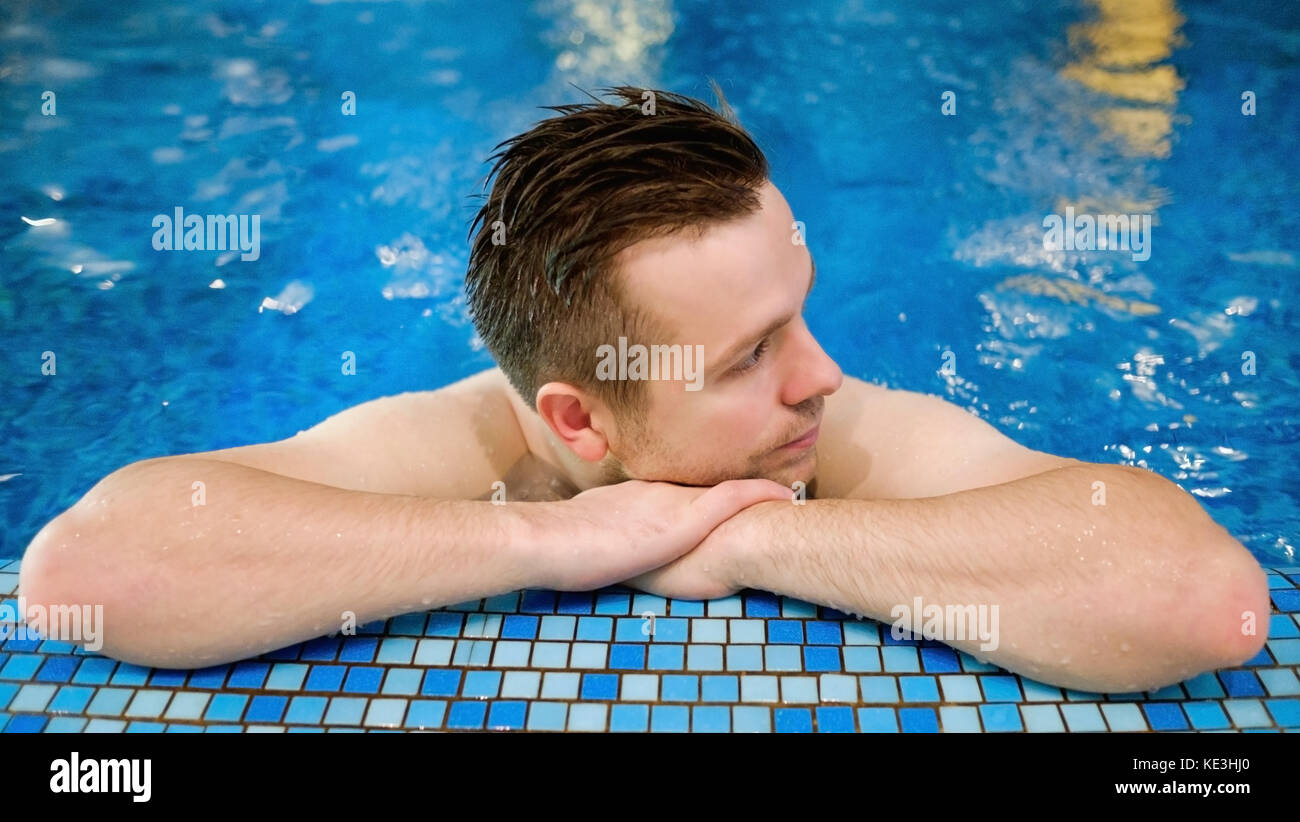 L'uomo è appoggiata sul bordo della piscina. Le mani vicino al mento. Foto Stock