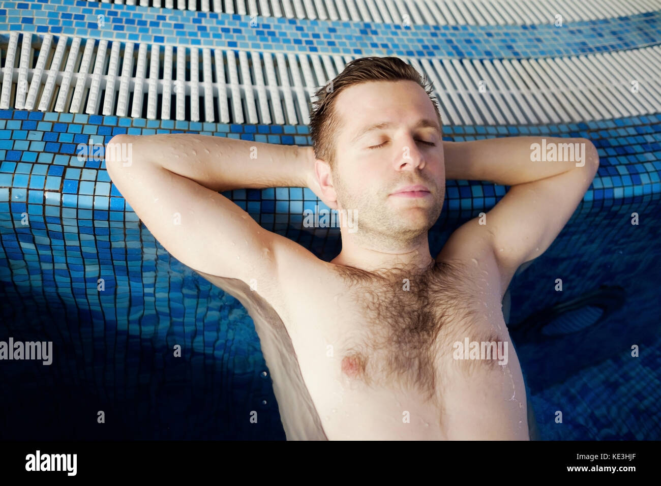 L'uomo è appoggiata sul bordo della piscina. Le mani sono dietro la testa. Foto Stock