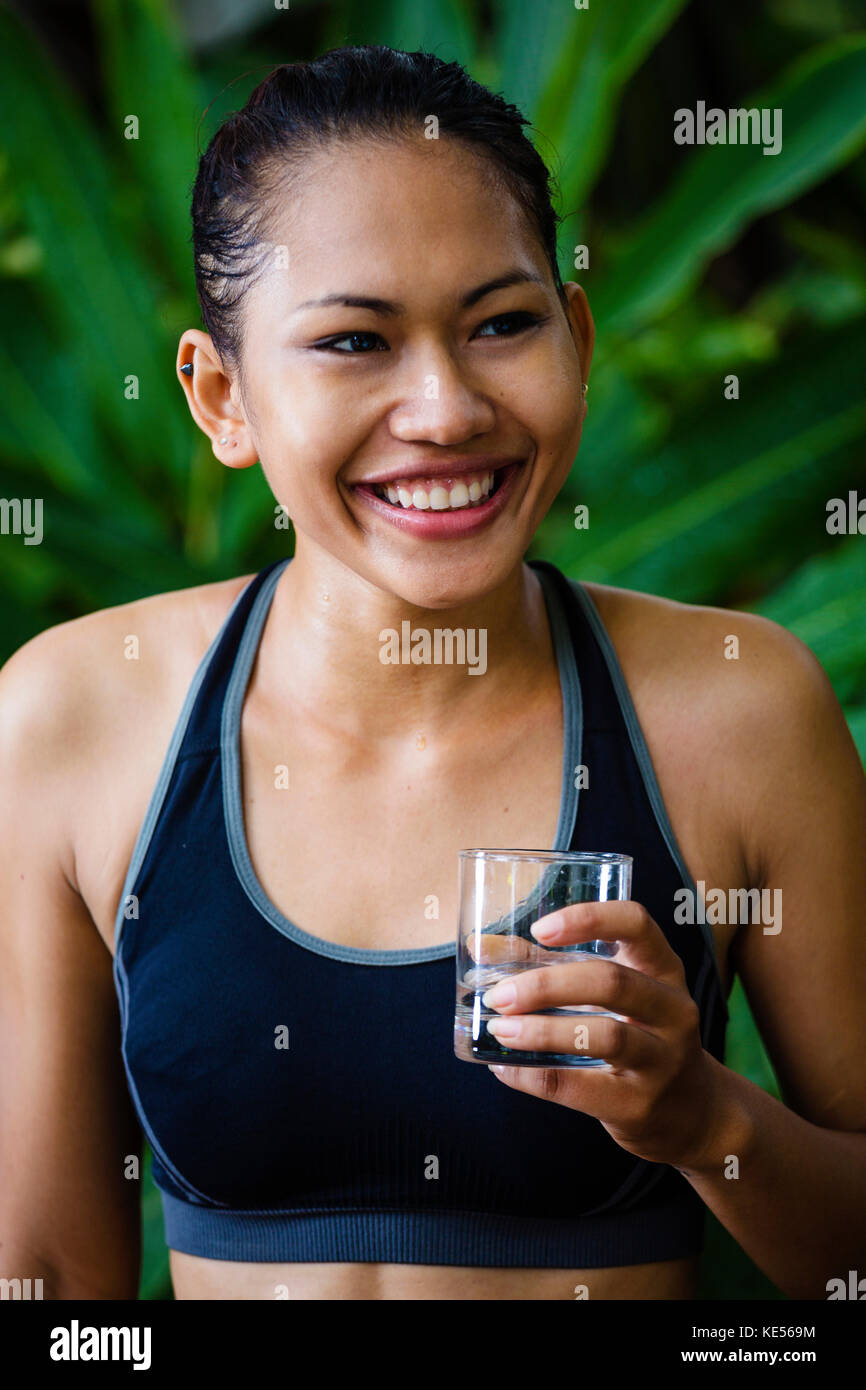 Donna asiatica in abiti di fitness con un bicchiere di acqua sorridente Foto Stock