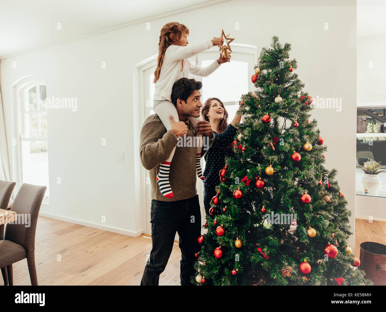 Famiglia decorare un albero di Natale. Giovane uomo con sua figlia sulle spalle di aiutarla a decorare l'albero di Natale. Foto Stock