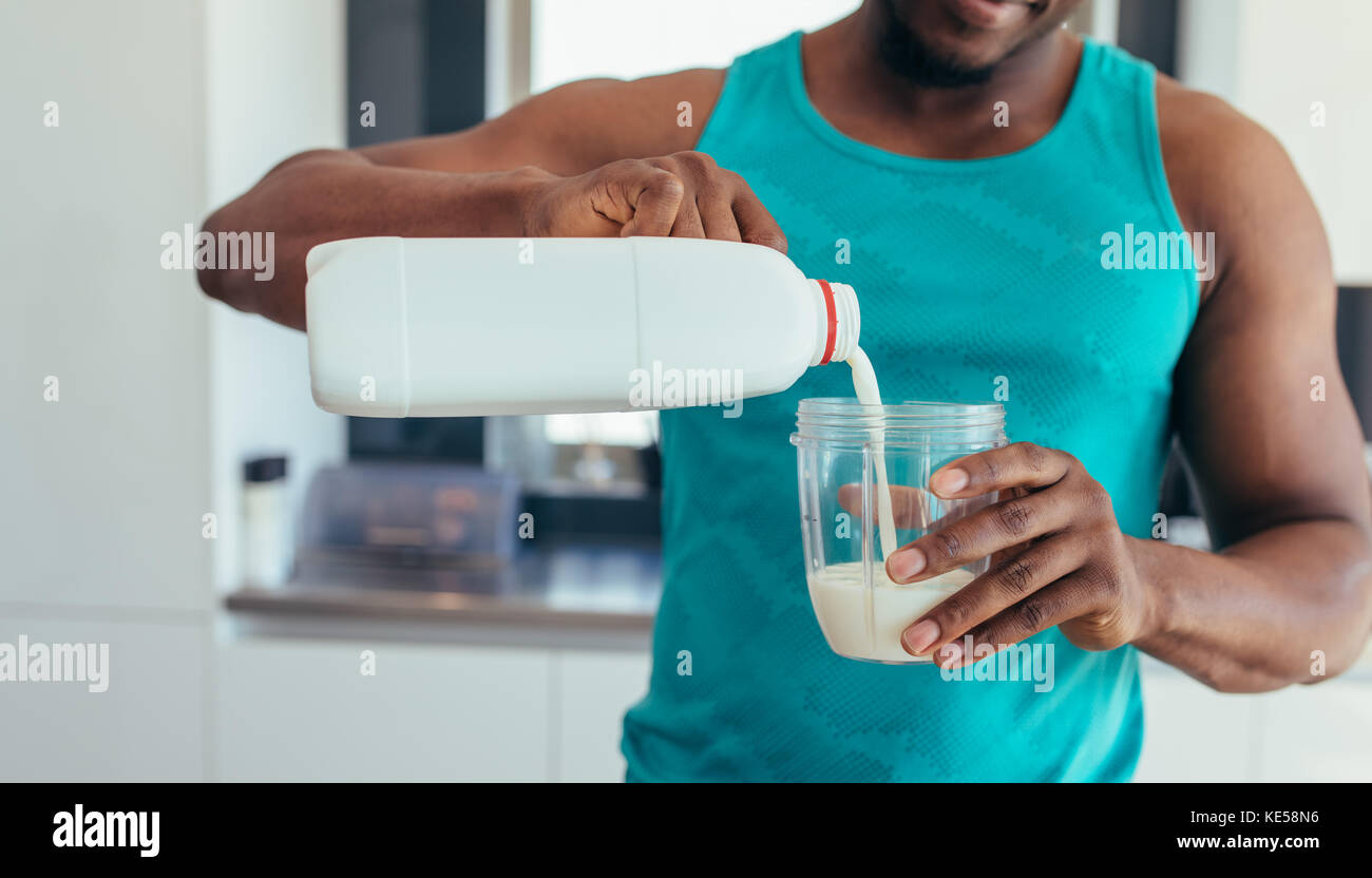 L'uomo versare il latte in un bicchiere dopo allenamento. Giovane uomo in cucina prepara la colazione. Foto Stock