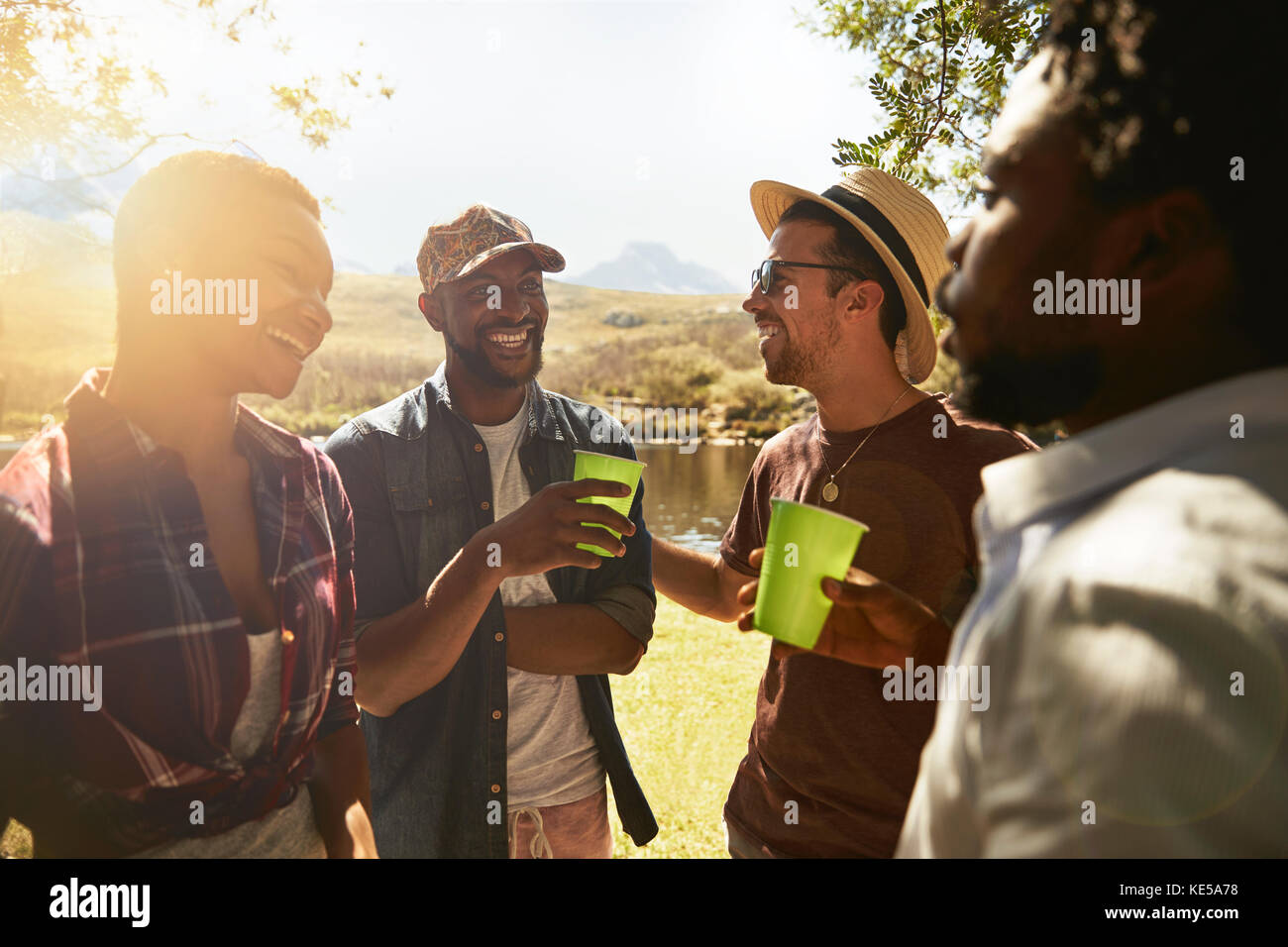 Giovani amici che bevono e si affacciano sul soleggiato lungofiume estivo Foto Stock