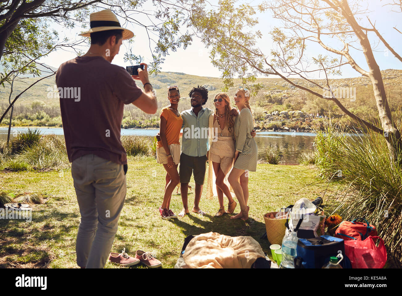 Giovane uomo che fotografa gli amici sulla soleggiata riva del fiume estivo Foto Stock