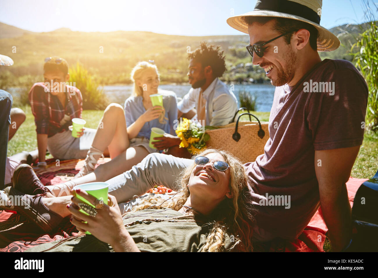 I giovani amici si rilassano, gustando un pic-nic in estate soleggiato lungofiume Foto Stock