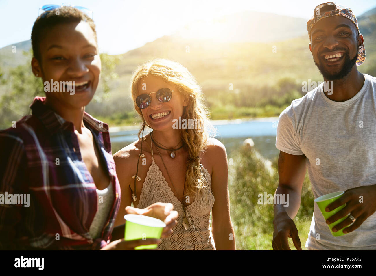 Ritratto entusiasta giovani amici che bevono al soleggiato lungofiume estivo Foto Stock