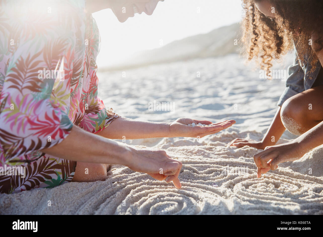 Madre e figlia disegnano spirali nella sabbia sul sole spiaggia estiva Foto Stock