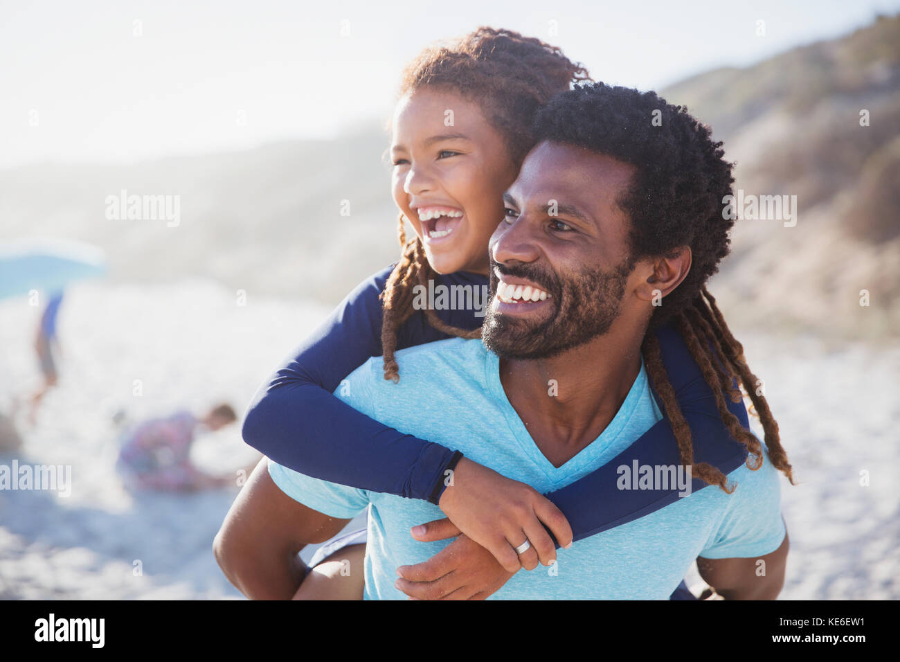 Ridendo padre piggybacking figlia sulla spiaggia soleggiata estiva Foto Stock