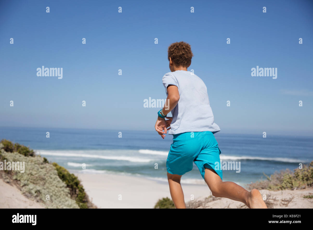 Ragazzo pre-adolescente che corre sulla soleggiata spiaggia estiva dell'oceano Foto Stock