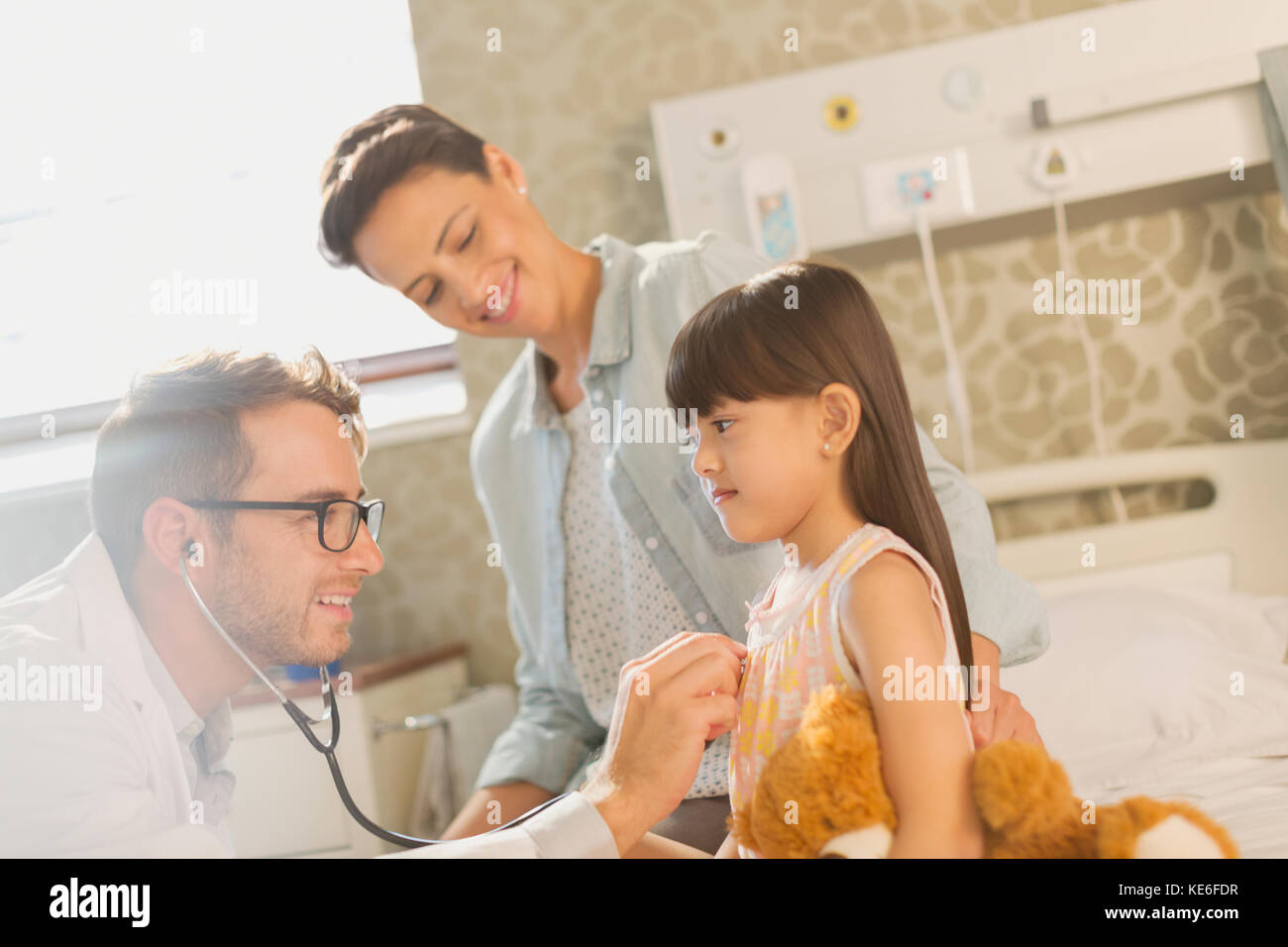 Medico di sesso maschile che usa stetoscopio su paziente di ragazza nella stanza dell'ospedale Foto Stock