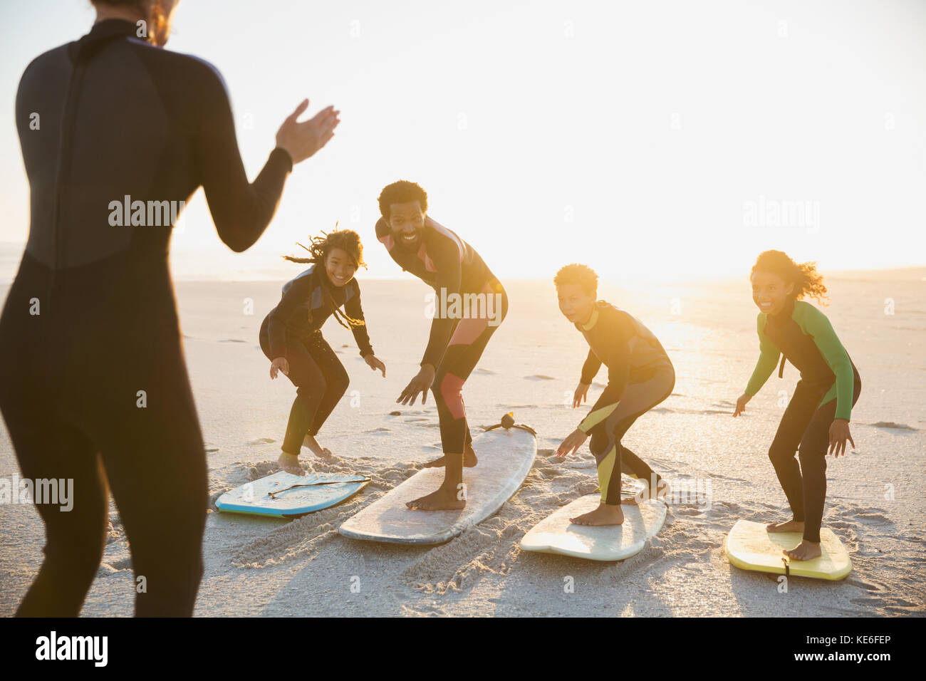 Istruttore di surf che insegna la famiglia sulle tavole da surf in estate soleggiato spiaggia del tramonto Foto Stock