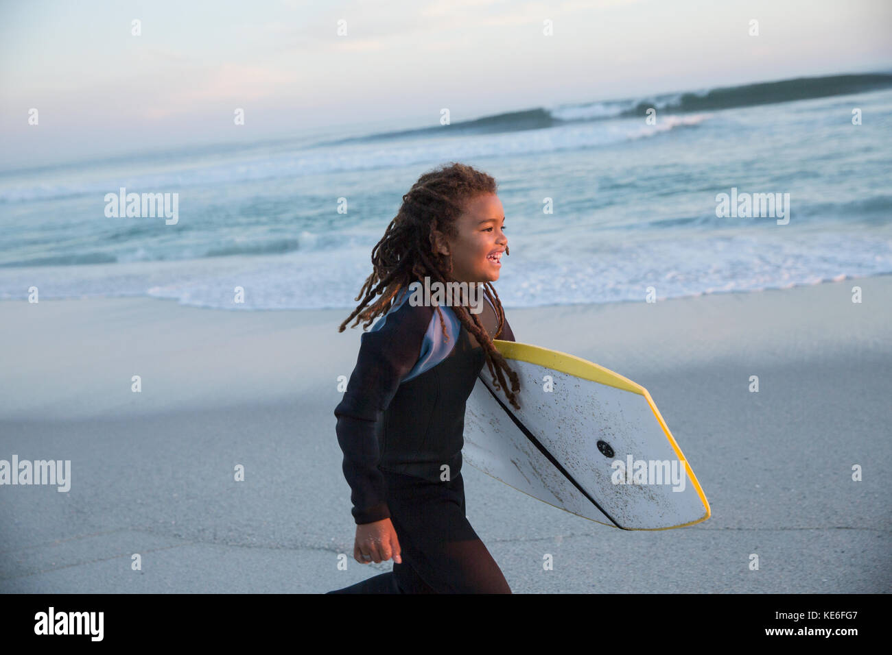 Ragazza sorridente pre-adolescente in tuta bagnata che corre con boogie board sulla spiaggia estiva Foto Stock