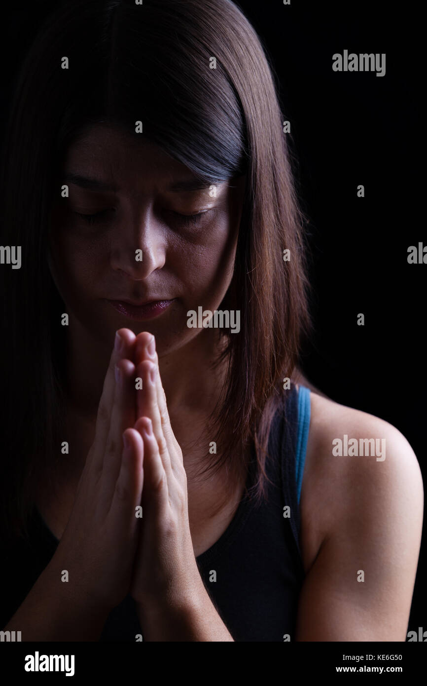 Fedeli athletic donna orante, mani piegate in adorazione a Dio, a testa in giù e gli occhi chiusi in fervore religioso. sfondo nero. preghiera pregare ritratto Foto Stock