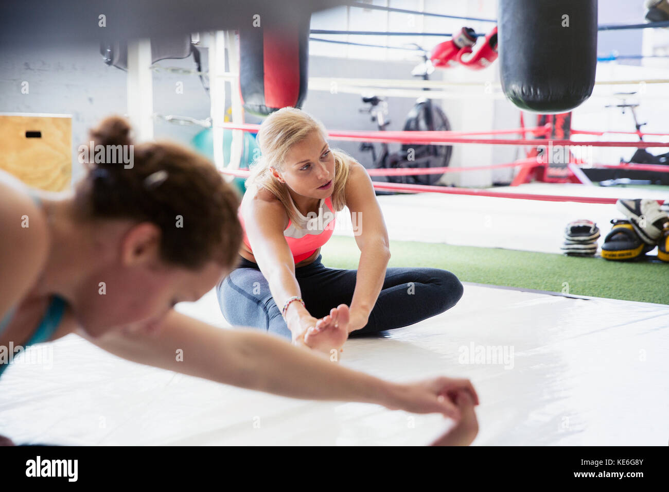 Le giovani donne allungano le gambe accanto all'anello di boxe in palestra Foto Stock