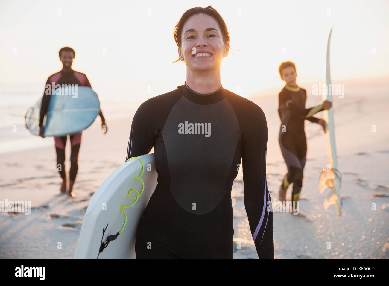 Ritratto sorridente surfista femminile in tuta bagnata con famiglia sulla soleggiata spiaggia estiva Foto Stock