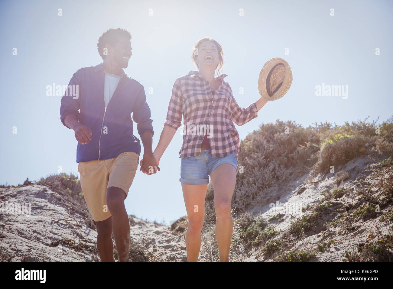 Coppia multietnica a piedi, tenendo le mani sul soleggiato sentiero estivo sulla spiaggia Foto Stock