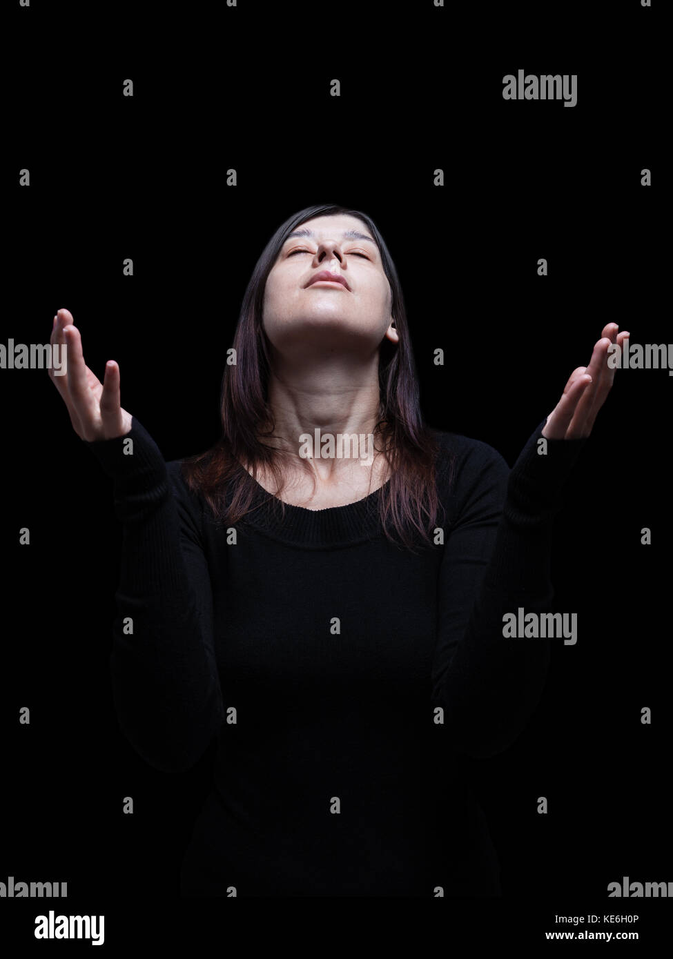 Lutto donna orante con le braccia aperte nel culto a Dio. cercando fino a occhi chiusi nella sofferenza. Sfondo nero / fede triste dolore lutto Foto Stock